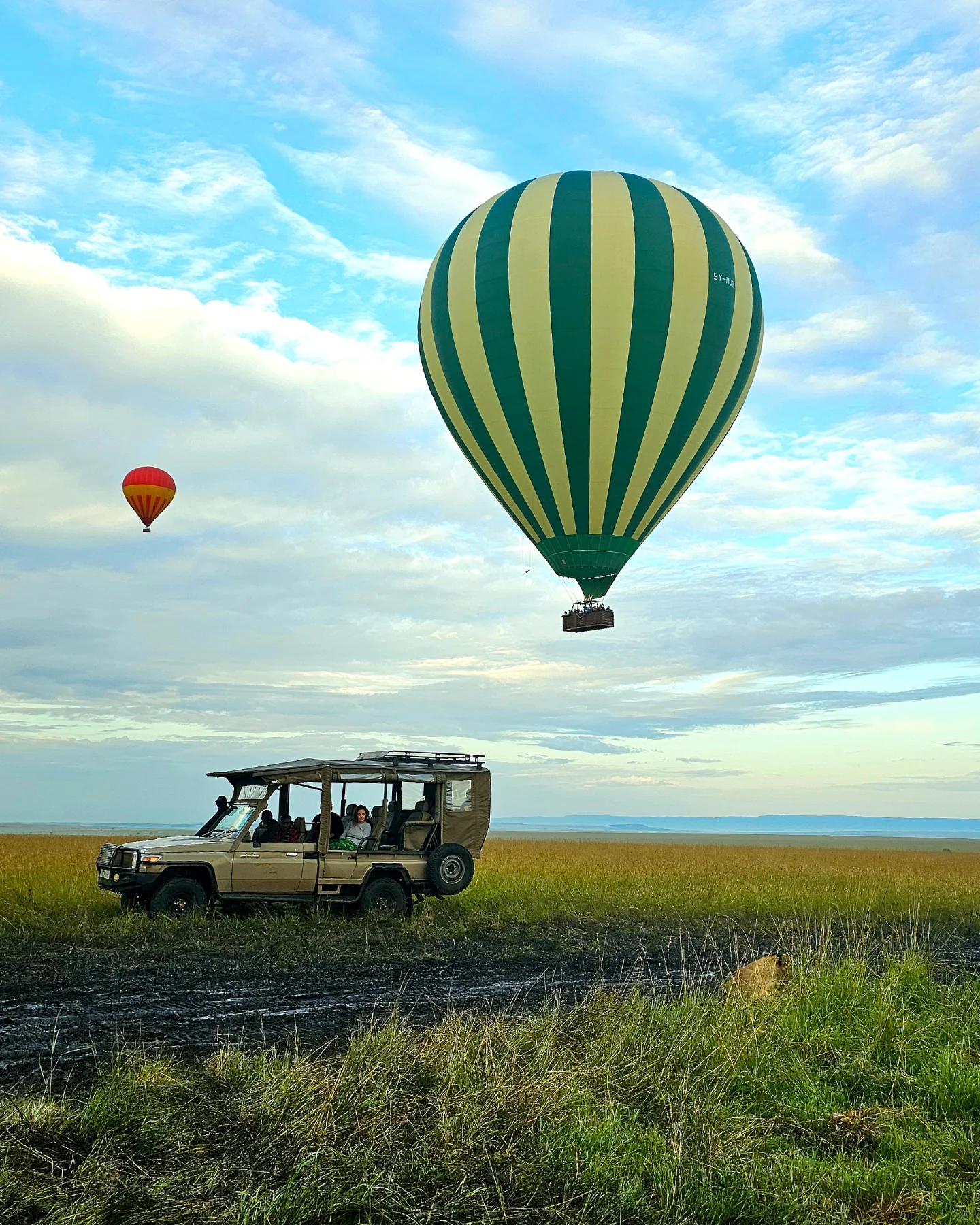 Hot-air balloons drifting over a safari jeep at dawn on the Masai Mara.