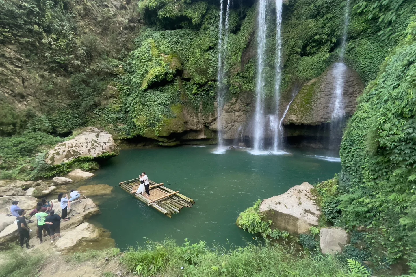 A couple on a bamboo raft beneath a jungle waterfall in Vietnam.